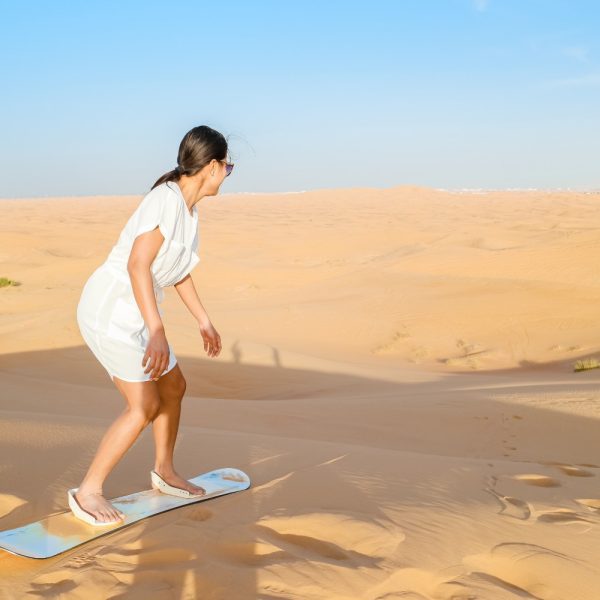 a lady enjoying the sandboarding over the dunes of Dubai desert